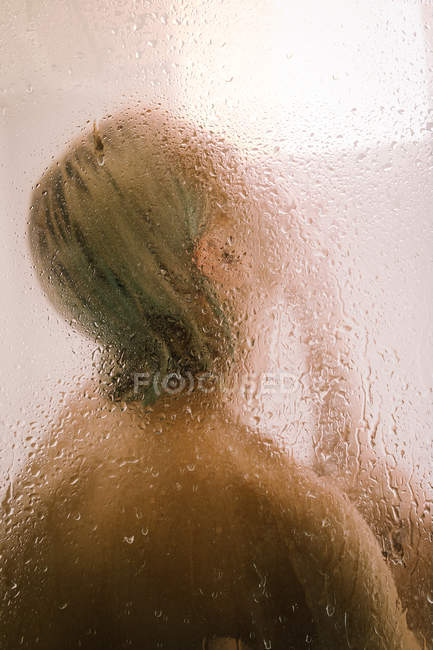 Vista lateral da jovem mulher tomando banho atrás da divisória transparente molhada no banheiro — Fotografia de Stock