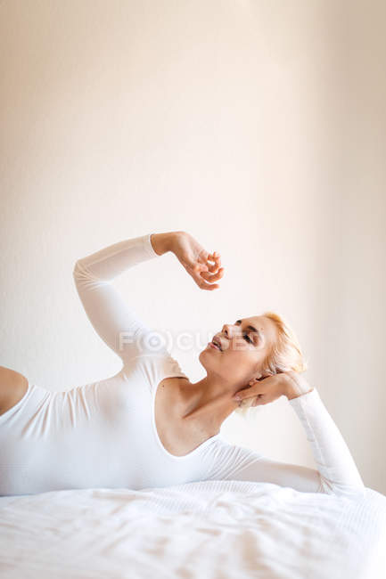 Mujer con el pelo rubio y en body apoyado en la mano y cerrando los ojos - foto de stock