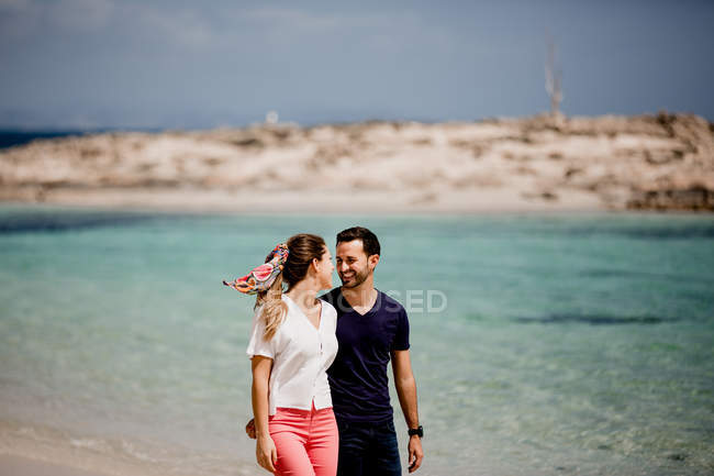 Happy couple walking on turquoise seashore in summer light — Stock Photo