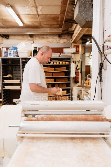 Crop man in latex glove and uniform decorating delicious cake with white cream swirls while working in bakery — Stock Photo