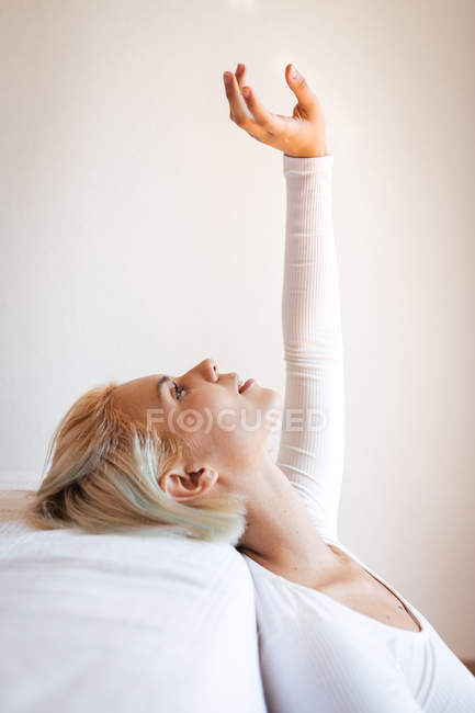 Vue latérale de belle dame blonde levant les yeux et s'appuyant sur un matelas confortable contre un mur blanc à la maison — Photo de stock