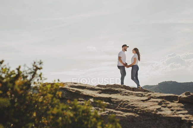 Пара влюбленных, держась за руки, стоя у горной скалы — стоковое фото