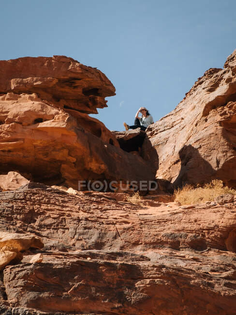 Снизу женщина-путешественница, сидящая на грубом скальном образовании против безоблачного голубого неба в пустыне Вади Рам в Иордании — стоковое фото