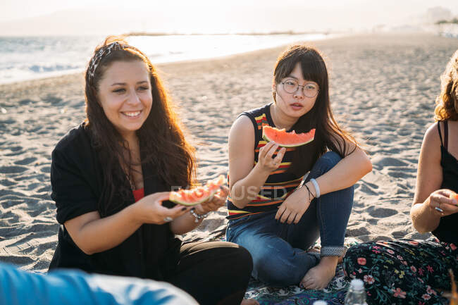 Duas mulheres pensativas na praia comendo melancia — Fotografia de Stock