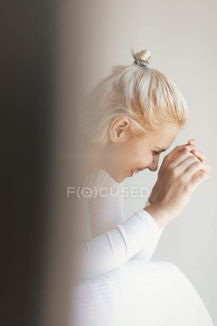 Cheerful young woman with blond hair and in bodysuit looking away while sitting on soft bed against white wall at home — Stock Photo