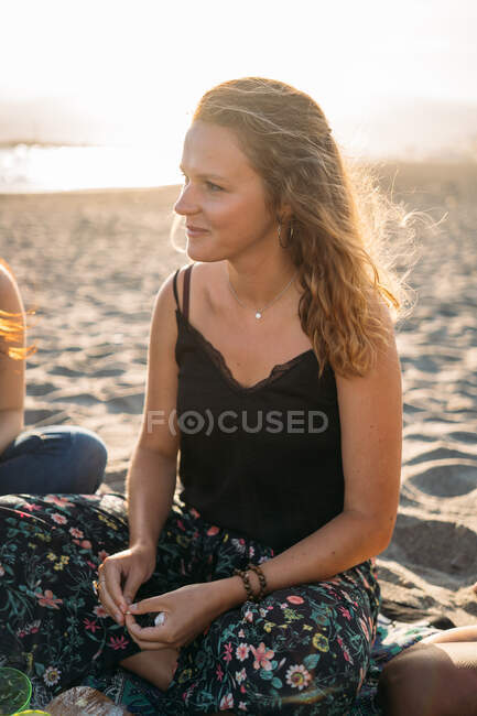 Красивая блондинка, сидящая на песке в пляжный день с солнцем за спиной — стоковое фото