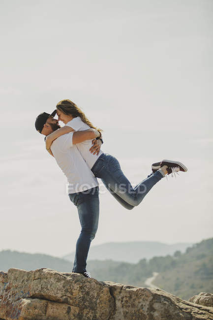 Amando casal abraçando enquanto está em pé no penhasco da montanha — Fotografia de Stock