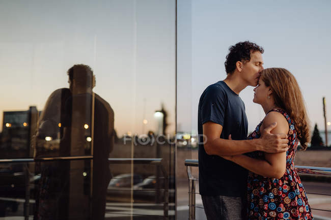 Вид збоку романтичної пари, що з'єднується на дорозі вздовж міської будівлі на сонячному світлі — стокове фото