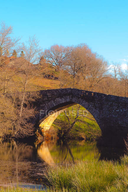 Envejecido puente de piedra sobre un río tranquilo en un día soleado en la pintoresca campiña de otoño - foto de stock