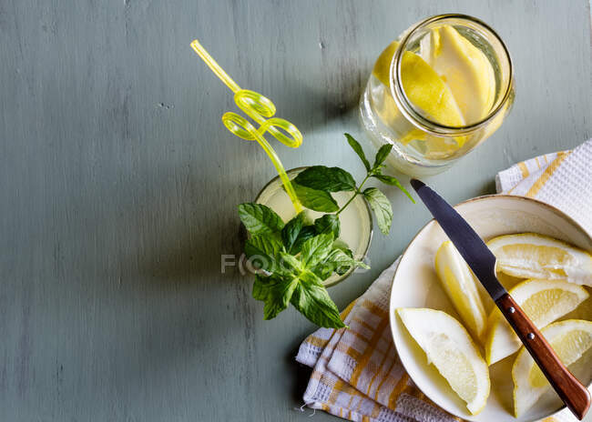Copa de limonada fresca junto al plato con limones cortados en la mesa - foto de stock