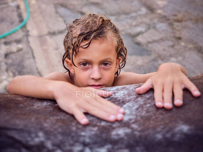 Happy shirtless kid with curly wet hair embracing horse side, leaning on belly on ranch — Stock Photo