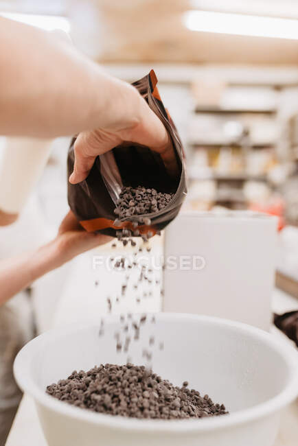 Trabajador irreconocible derramando callets de chocolate en un tazón antes de derretirse mientras trabaja en una panadería - foto de stock