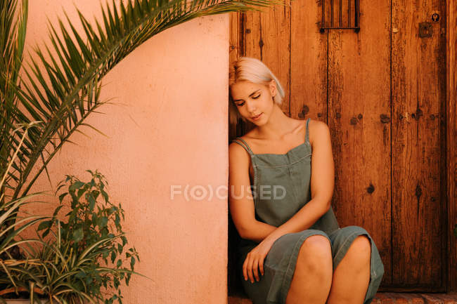 Young woman with closed eyes sitting near wooden door and plants in yard — Stock Photo