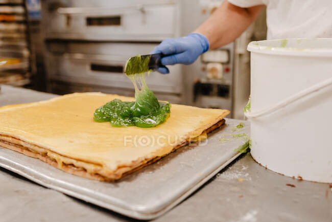 Unrecognizable confectioner putting yummy kiwi jelly from bucket on cake base while preparing pastry in bakery kitchen — Stock Photo
