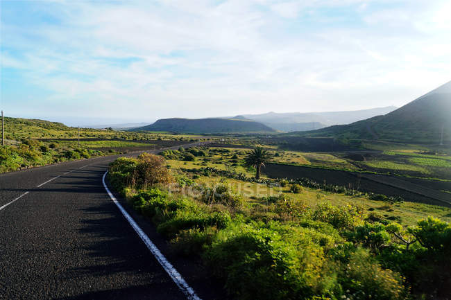 Route vide à pied vers la vallée de montagne le long du champ avec verdure à Lanzarote Îles Canaries Espagne — Photo de stock