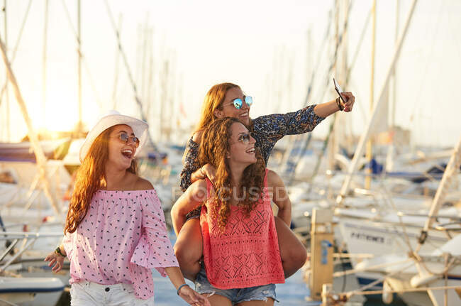 Woman carrying girlfriend on back and taking selfie — Stock Photo