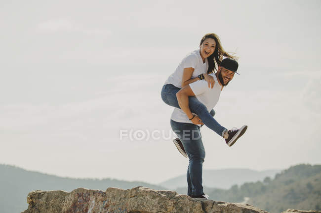 Lovely man holding woman on back at mountain cliff — Stock Photo