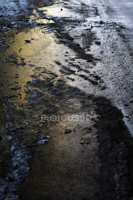 Traço de roda na estrada de asfalto com neve derretida lamacenta no crepúsculo — Fotografia de Stock