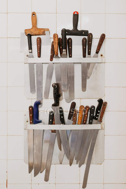Держатели с различными ножами и лопатками, висящими на черепичной стене в пекарне — стоковое фото