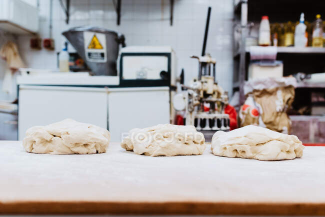 Кучи свежего пшеничного теста на муковом столе на размытом фоне хлебопекарной кухни — стоковое фото