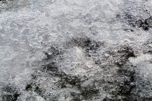 Schmelzen von Eis und Schnee auf felsiger Oberfläche mit Kieselsteinen bei Tageslicht — Stockfoto