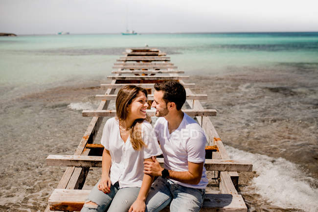 Amoureux heureux assis sur jetée détruite sur le bord de la mer — Photo de stock