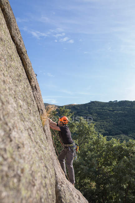 De baixo do homem escalando uma rocha na natureza com equipamento de escalada — Fotografia de Stock