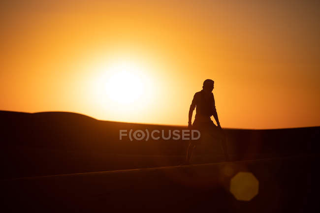 Side view of unrecognizable tourist with outstretched arms standing against bright cloudless sundown sky in desert — Stock Photo