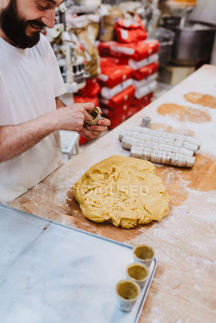 Crop man en t-shirt blanc mettre de la pâte fraîche dans les tasses tout en faisant de la pâtisserie dans la cuisine de la boulangerie — Photo de stock