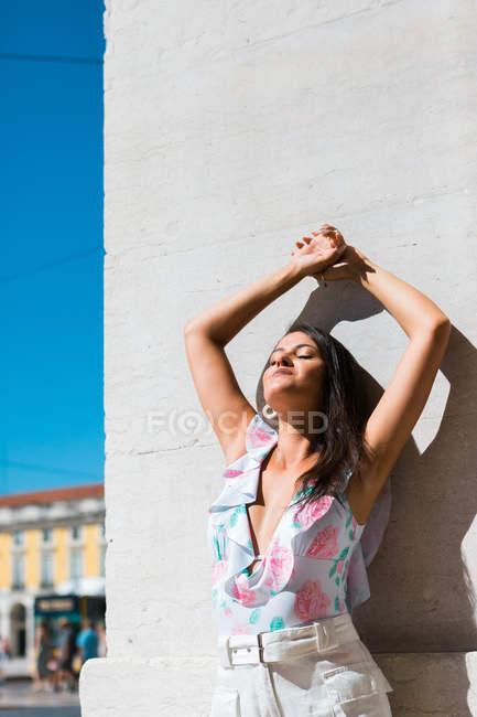 Peaceful gorgeous woman in trendy outfit standing on white wall with hands up on scenic street — Stock Photo