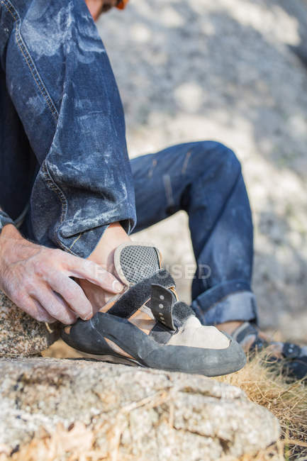 Imagen recortada de escalador de roca poniéndose sus zapatos de escalador para empezar a escalar - foto de stock