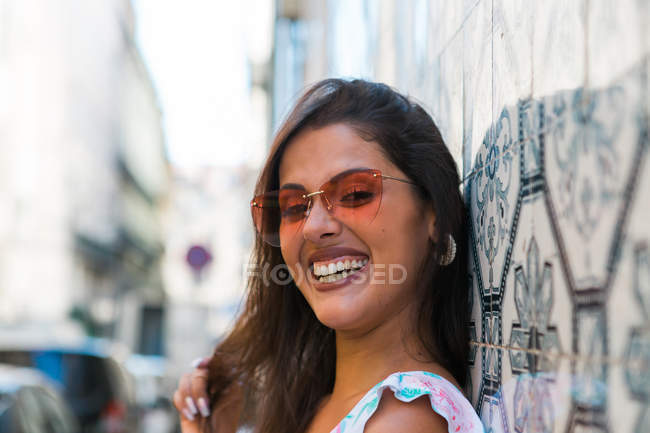 Peaceful gorgeous woman in trendy outfit and shiny sunglasses leaning on tiled exotic wall on scenic street — Stock Photo