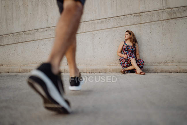 Жінка сидить на сірій стіні, поки людина врожаю йде до неї — стокове фото