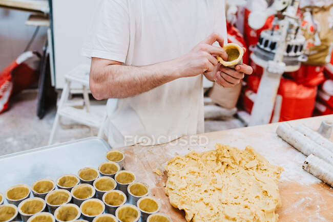 Unrecognizable man putting nuts on top of sweet small cakes while working in bakery — Stock Photo