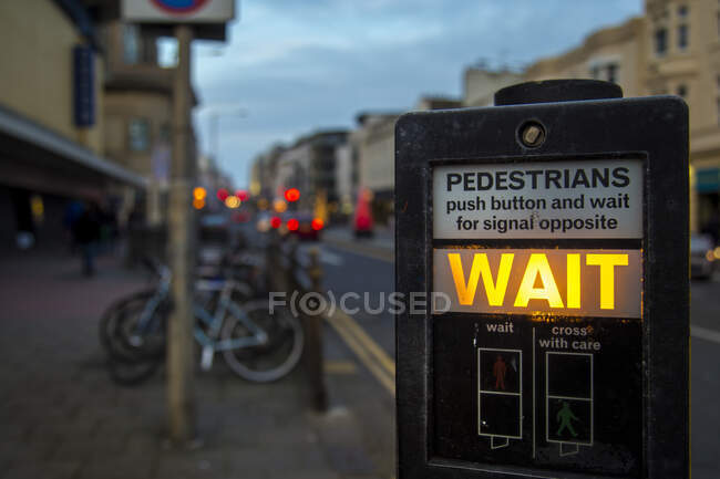 Painel de instruções moderno para semáforo com sinal de espera brilhante no fundo borrado da rua da noite em Brighton, Inglaterra — Fotografia de Stock