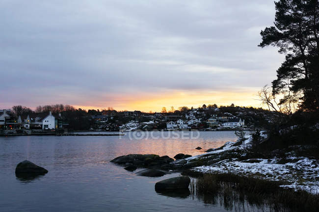 Idilliaco lungomare con distanti edifici cittadini sul fondo della collina con tranquilla acqua increspata del lago alla luce del tramonto — Foto stock