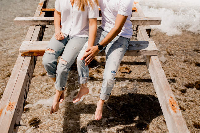 Imagem cortada de amantes sentados no cais destruído na praia — Fotografia de Stock
