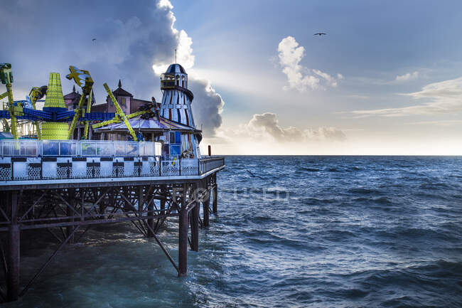 Attrazioni colorate del parco divertimenti sul molo vicino al mare che ondeggia contro il cielo nuvoloso in serata a Brighton, Inghilterra — Foto stock