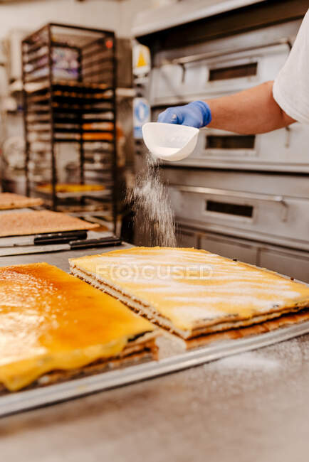 Anonymer Koch verschüttet Zuckerpulver aus Schaufel auf leckeren Kuchen, während er in der Küche der Bäckerei arbeitet — Stockfoto
