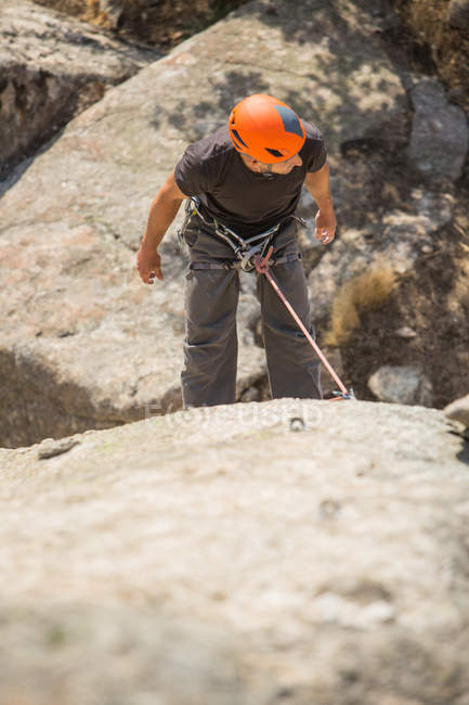 Desde arriba el hombre escalando una roca en la naturaleza con equipo de escalada - foto de stock