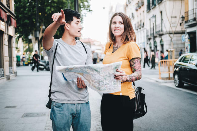 Positivo ridere persone multietniche in cerca di direzione sulla mappa mentre in piedi sulla strada della città — Foto stock