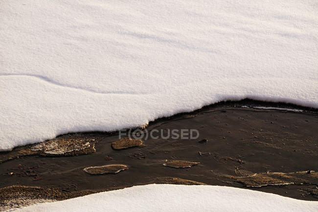 Thawing hole in melting ice layer with snow covering water stream in spring — Stock Photo
