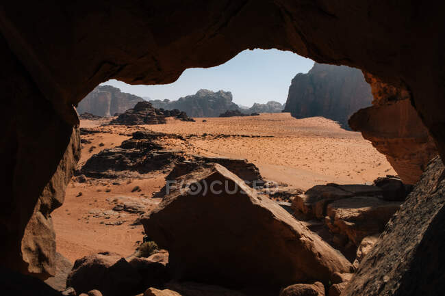 Sandy Wadi Rum valley near entrance of rocky cave on sunny day in Jordan — Stock Photo