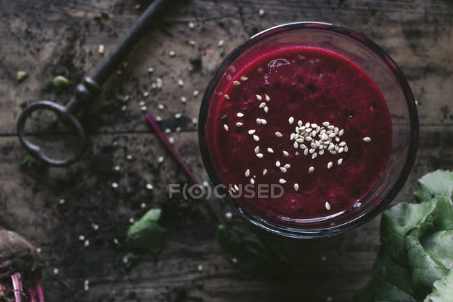 Glass of organic delicious beetroot smoothie with sesame seeds on wooden table with vintage key — Stock Photo