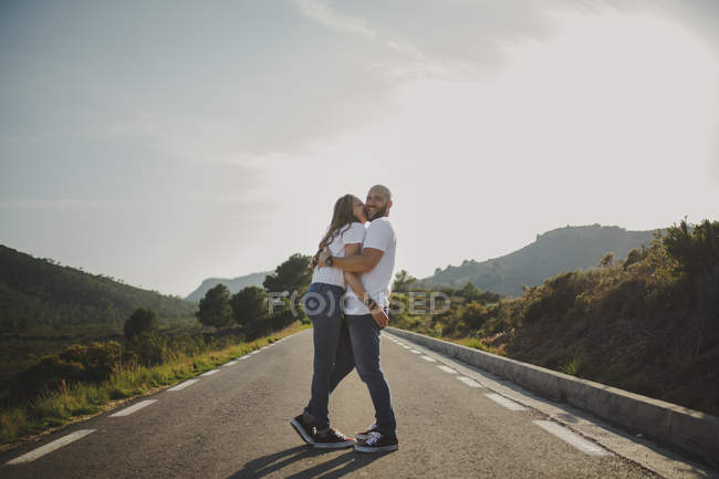 Прихильна пара обіймається, стоячи на сільській дорозі — стокове фото