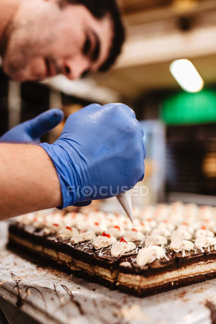 Anonymous cook squeezing fresh pastry dough on tray with paper while working on blurred background of bakery — Stock Photo