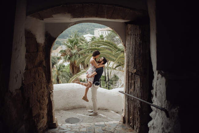 Ласковая пара обнимается, стоя на улице в старой арке тропического города — стоковое фото