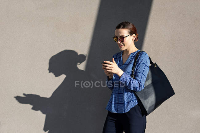 Mujer emprendedora alegre en chaqueta elegante sonriendo y usando teléfono inteligente - foto de stock