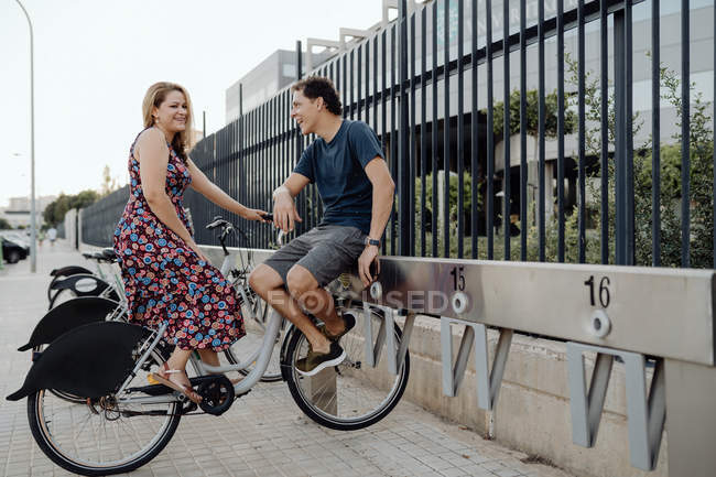Vista lateral do casal romântico conversando ternamente enquanto sentado em bicicleta e ter descanso nas proximidades cerca ornamental durante a caminhada — Fotografia de Stock