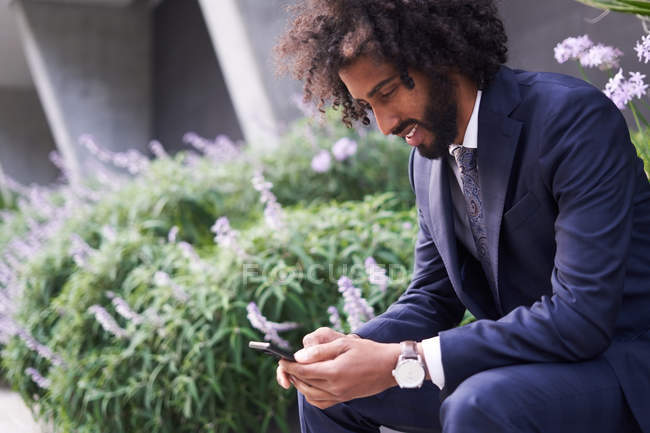 Freudiger afrikanisch-amerikanischer Mann im Anzug sitzt draußen und sendet Nachrichten — Stockfoto